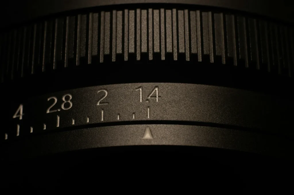 Close-up of a camera lens focus ring with engraved numbers, including 1.4, 2, 2.8, and 4. The lighting highlights the textured grip.