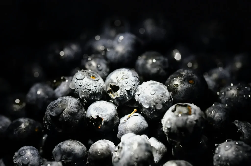 Close-up of fresh blueberries covered in water droplets, glistening under soft light. The deep blue tones convey a fresh, juicy, and appetizing feel