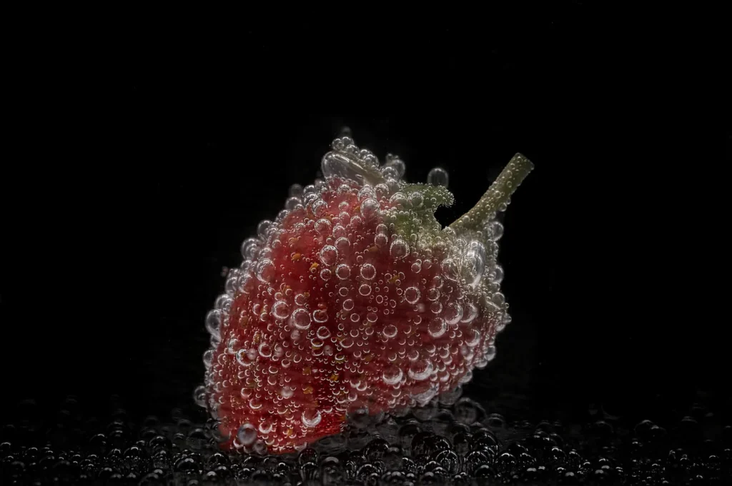 “A strawberry covered in bubbles is set against a black background. The close-up highlights the texture and freshness, with a crisp, vibrant feel.”