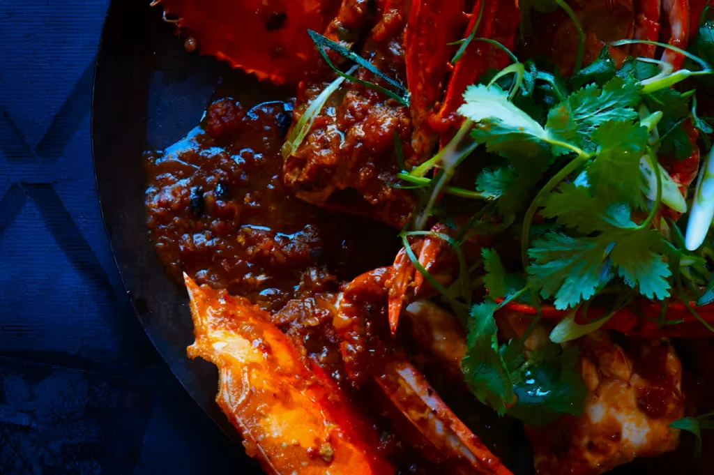 A rich, spicy crab curry is presented on a dark plate, garnished with fresh cilantro and green onions. The vibrant colors evoke a mouthwatering appeal.
