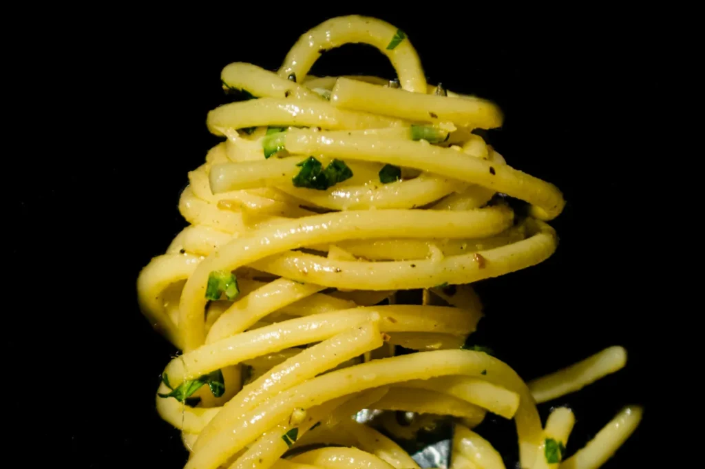 Close-up of neatly twirled spaghetti with a light olive oil and parsley garnish set against a dark background, creating a fresh, inviting look.