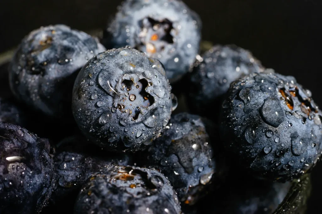 “Close-up of fresh blueberries with glistening water droplets on the surface, creating a refreshing and appetizing look against a dark background.”