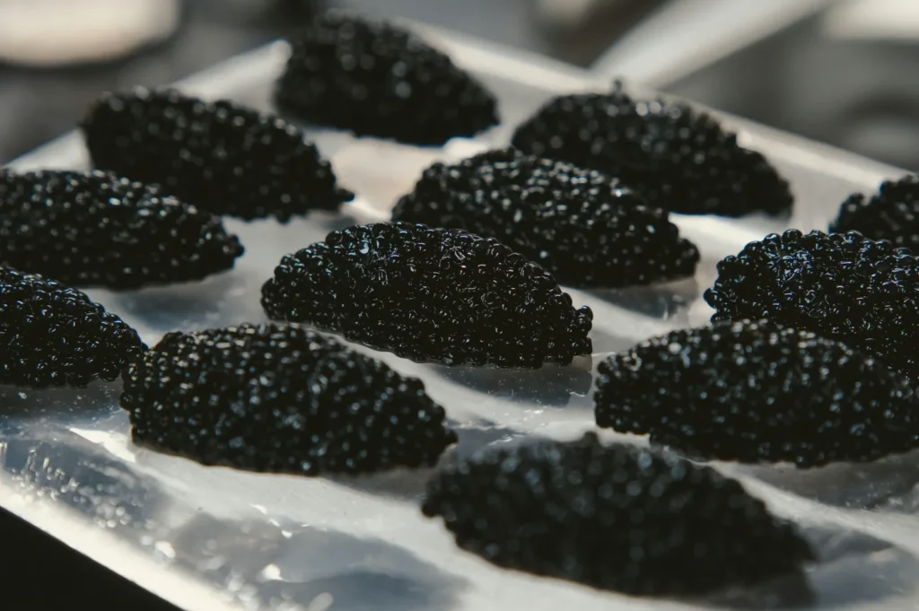 Close-up of several small black caviar mounds on a reflective metal tray, creating a luxurious and sophisticated atmosphere.