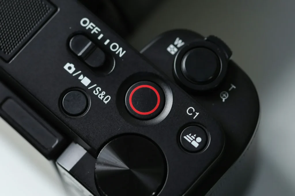 Close-up of a camera's control panel featuring an on/off switch, a red video record button, and white icons. The tone is sleek and modern.