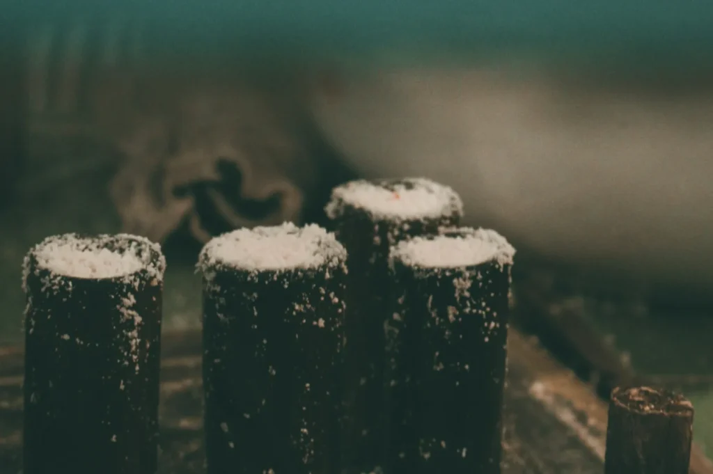Close-up of traditional cylindrical pastries dusted with powdered sugar, set on a rustic wooden board. The background is softly blurred, creating a cozy ambiance.