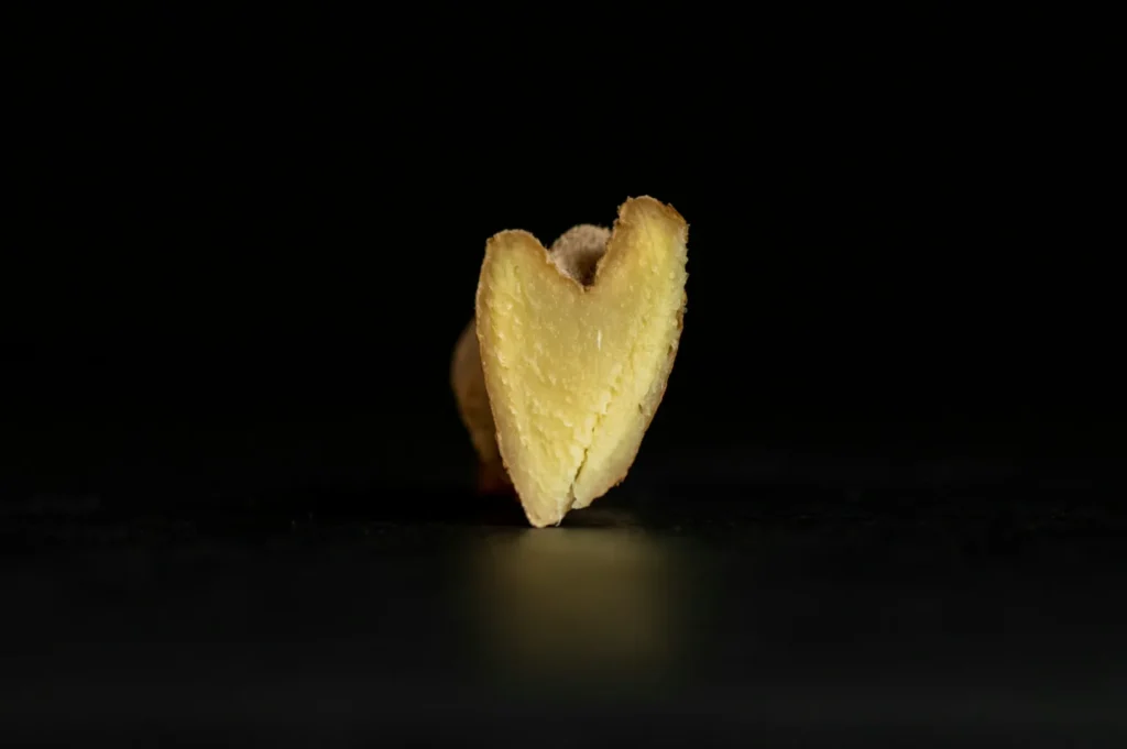 A close-up of a heart-shaped, golden-brown cookie stands upright against a black background. The cookie texture is crumbly, creating a warm, inviting feel.