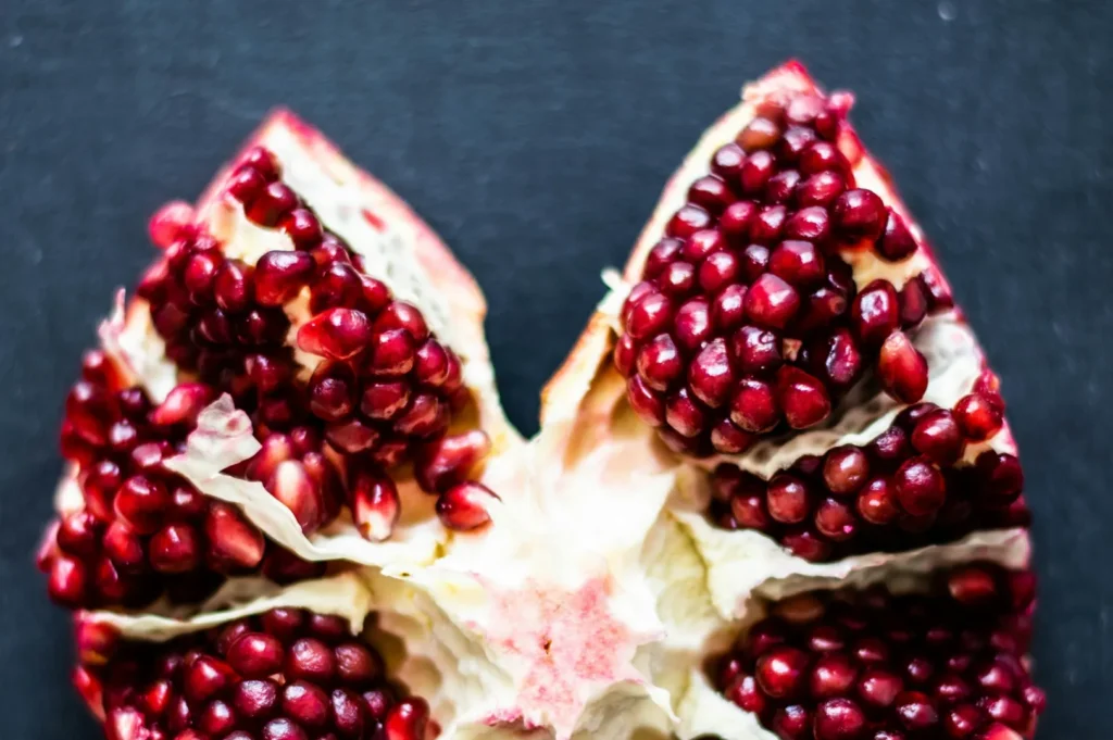 Close-up of an open pomegranate showing vibrant red seeds against a dark background. The juicy seeds contrast with the creamy white pith, creating a fresh, inviting look.