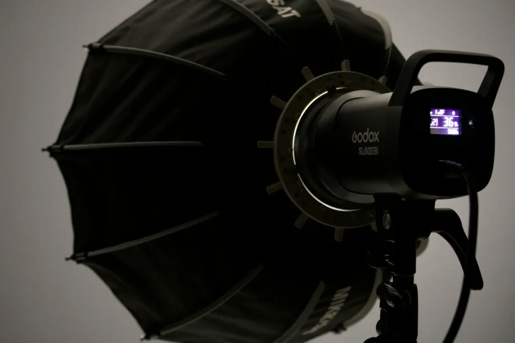 Studio lighting setup with a black octagonal softbox attached to a Godox SL60Bi continuous LED light. The dimly lit scene suggests a professional photography setting.