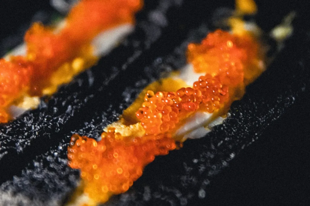 Close-up of vibrant orange fish roe on black nori, with a textured surface creating a contrasting backdrop, exuding a fresh, gourmet appeal.