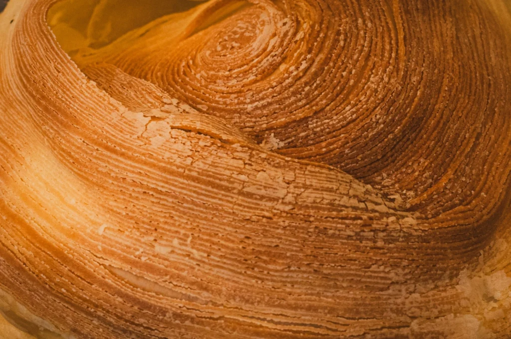 Close-up of a flaky, golden-brown pastry with swirling, textured layers. The intricate pattern suggests warmth and rich, buttery flavor.