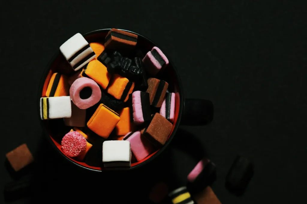 A top view of a mug filled with colorful licorice allsorts candies in shades of pink, orange, and brown, against a dark background.