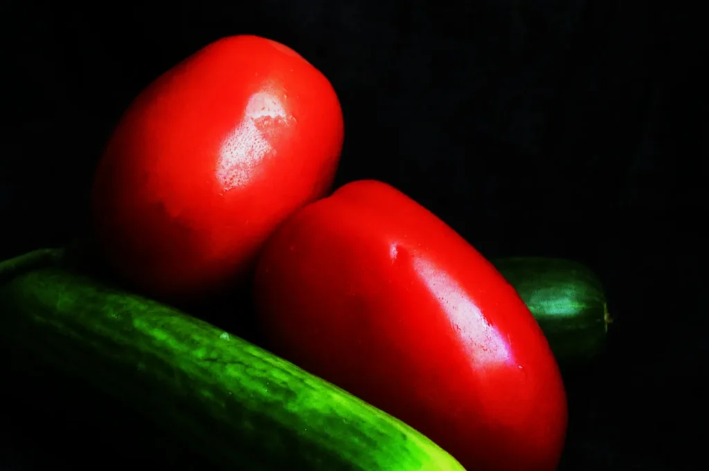 Two vibrant red tomatoes rest on a fresh green cucumber against a dark background, creating a striking contrast and highlighting their glossy surfaces.