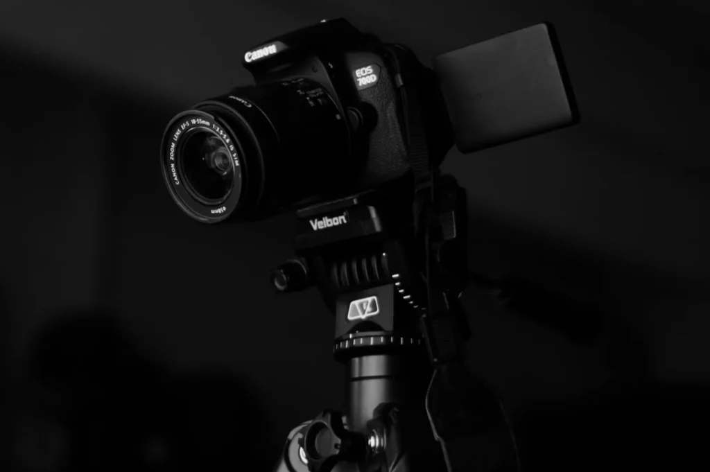 “Close-up of a Canon EOS 700D camera mounted on a Velbon tripod, captured in a dimly lit setting. The mood is focused and technical.”