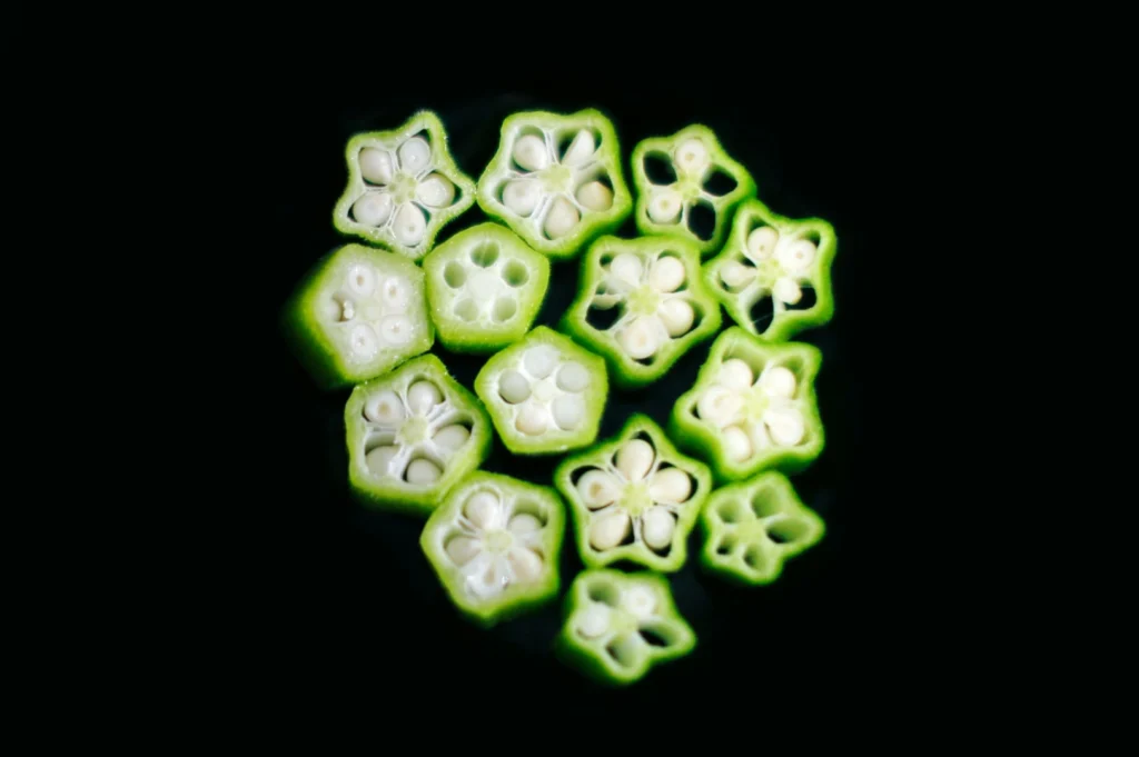 “Close-up of sliced okra on a black background, revealing star-shaped cross-sections with white seeds. The bright green edges contrast sharply.”