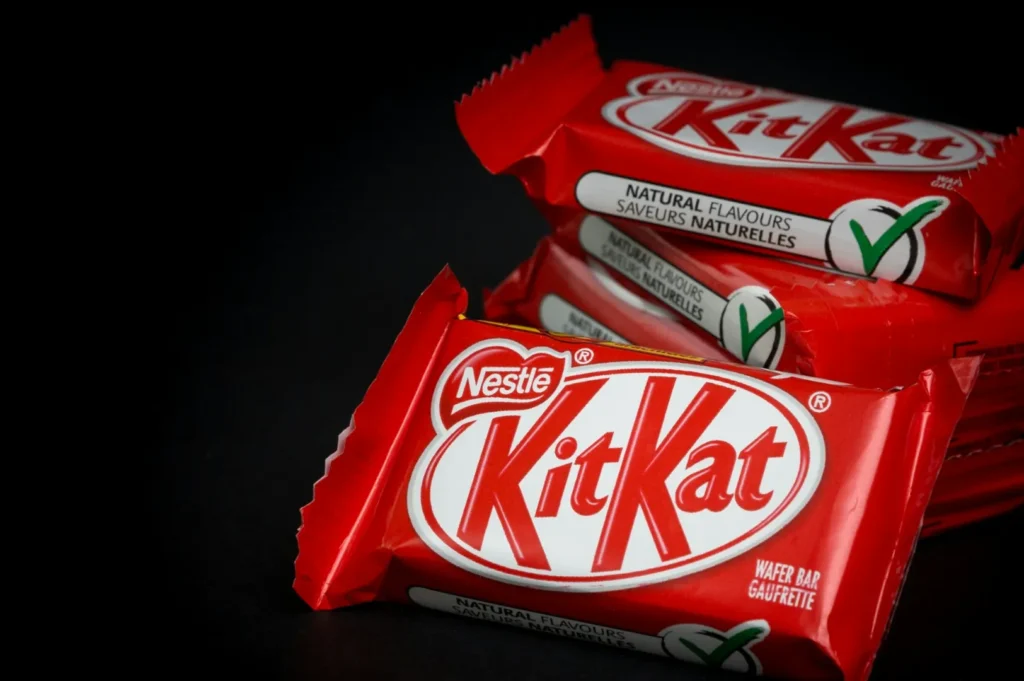 “Close-up of three red KitKat wrappers on a black background. The image conveys a sense of indulgence and invites a chocolate craving.”