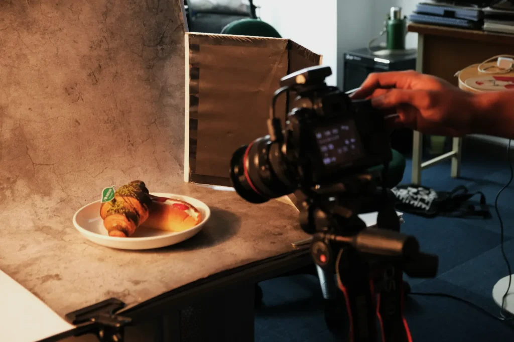 “A camera captures pastries on a plate in a studio setup with a textured backdrop and lighting. The scene conveys a professional food photography vibe.”