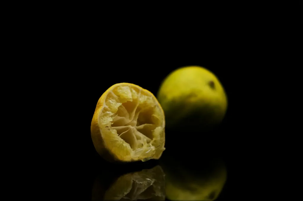 “A halved lemon and a whole lemon are placed on a reflective black surface, highlighting their vivid yellow color and casting subtle reflections.”