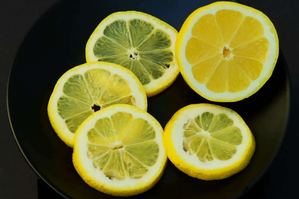 “Slices of lemon laid out on a black plate, showcasing vibrant yellow hues and a fresh, tangy appearance. The arrangement is simple and artistic.”