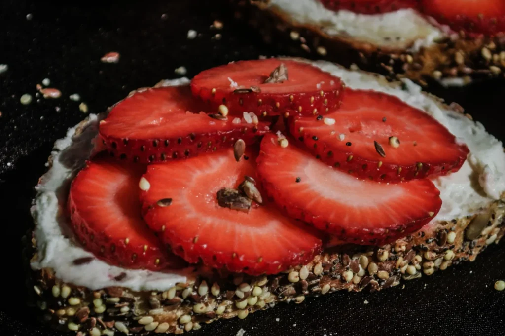 “Close-up of sliced strawberries on a multigrain bread topped with creamy spread. The seeds on the crust add texture; the mood feels fresh and tempting.”