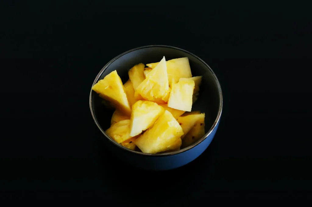 “A bowl filled with fresh, juicy pineapple chunks sits against a dark background, emphasizing the vibrant yellow color and inviting texture of the fruit.”