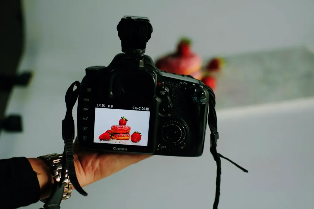 “A digital camera displays a close-up of a dessert stack topped with strawberries, suggesting a food photography session. The mood is artistic and focused.”