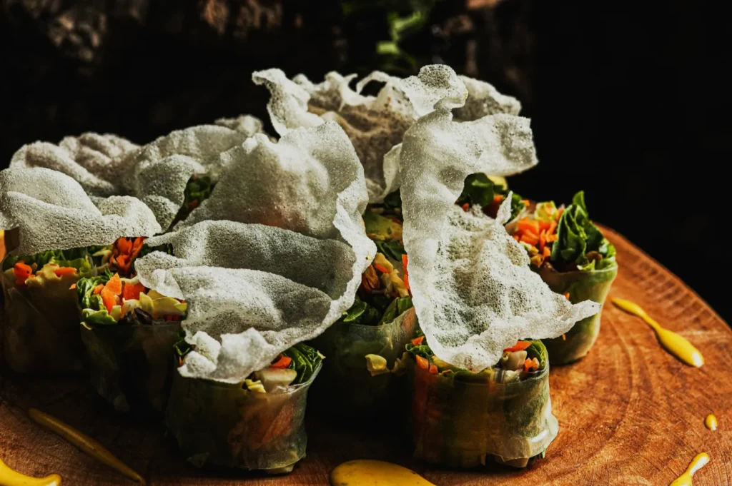 Close-up of fresh spring rolls cut in halves, filled with colorful vegetables and topped with delicate, crispy rice paper, on a wooden board.