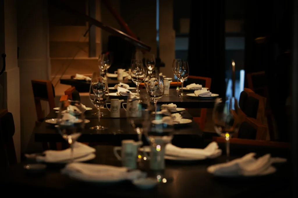 Dimly lit, elegant restaurant with neatly set tables. Glasses and folded napkins create a sophisticated, inviting ambiance. Warm, intimate mood.