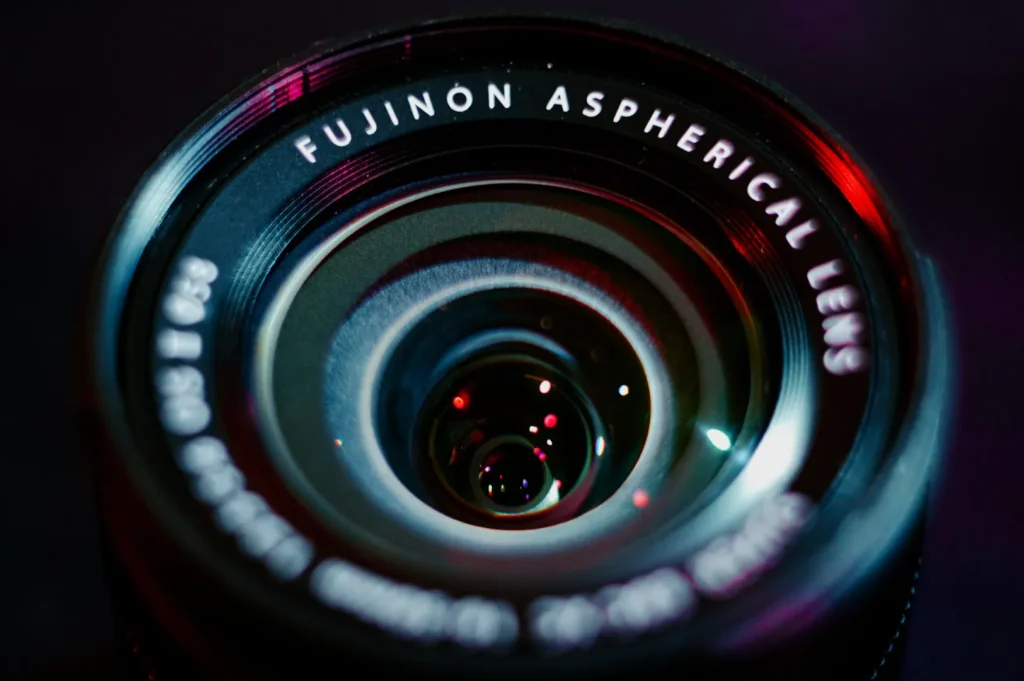 “Close-up of a Fujinon Aspherical Lens with reflective surface. The lens glistens with red and blue light, conveying precision and elegance.”