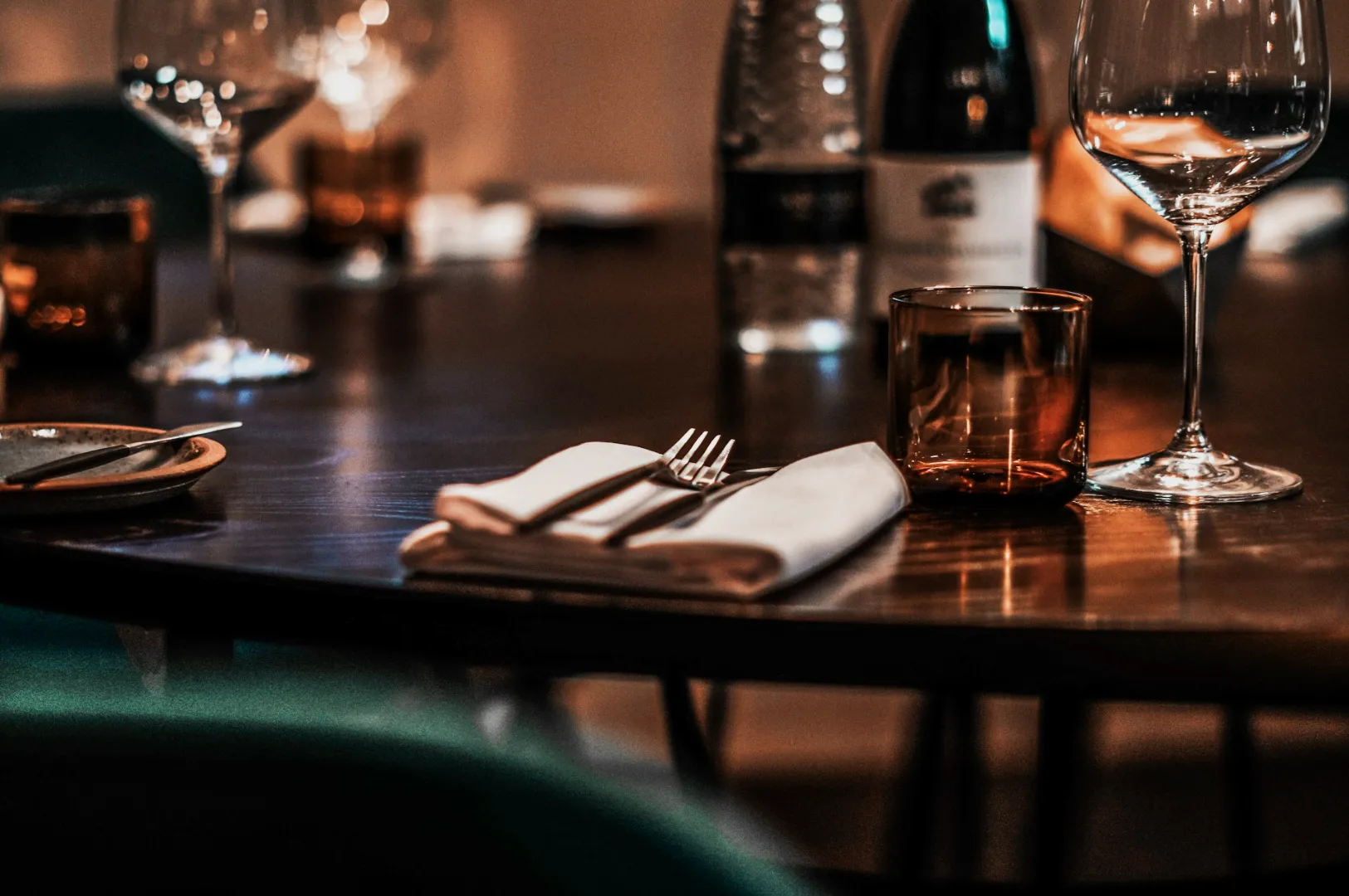 Elegant dining table set with wine glasses, a folded napkin, and cutlery. Dim lighting creates a cozy and inviting atmosphere.