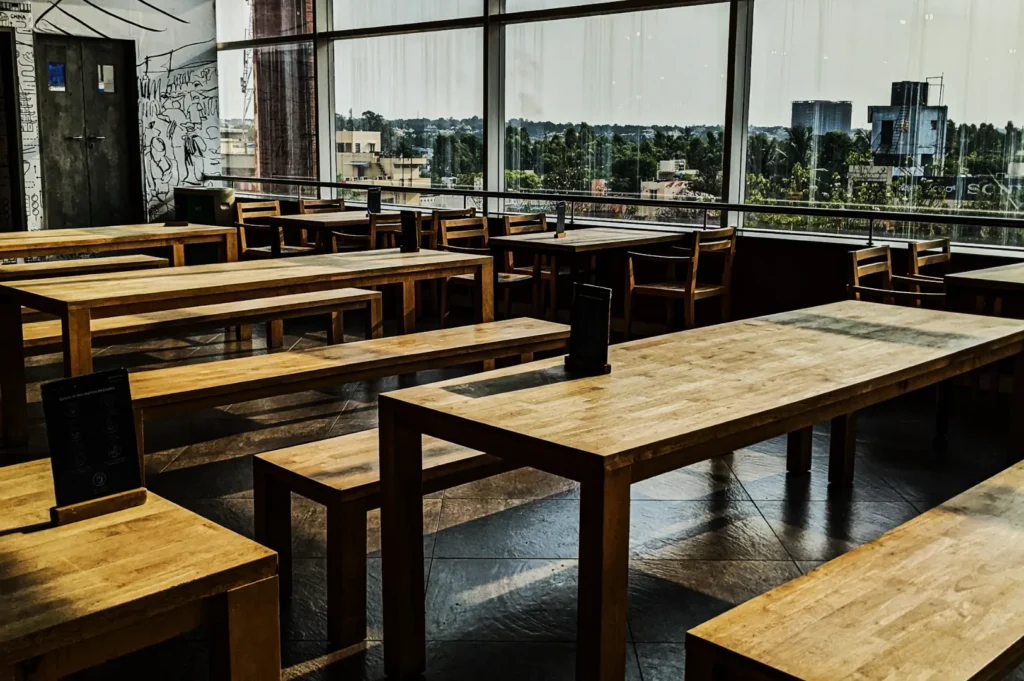 Spacious cafe with wooden tables and benches, large windows reveal a cityscape view. Soft, natural lighting creates a calm, inviting atmosphere.