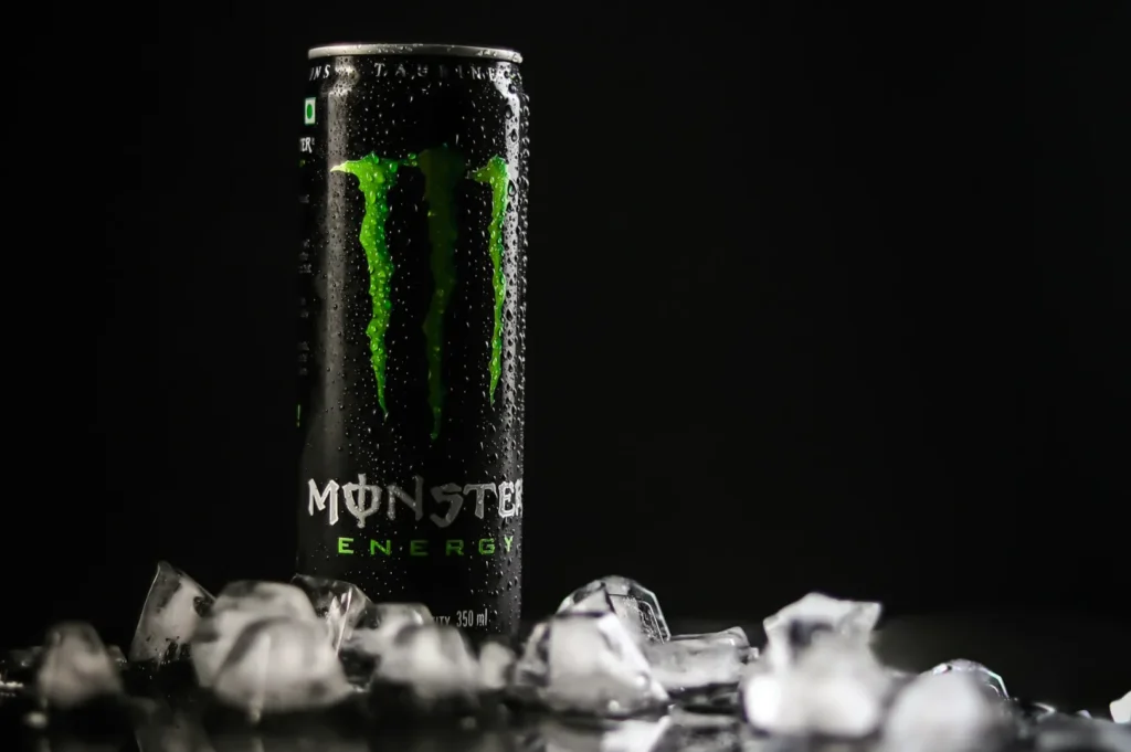 A can of Monster Energy, wet with condensation, stands against a black background, surrounded by melting ice cubes, conveying a refreshingly cool vibe.