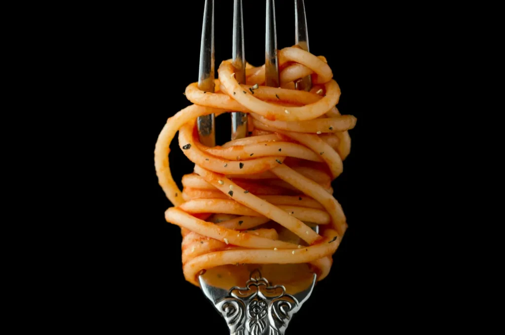 Close-up of a silver fork with ornate detailing, wrapped tightly with spaghetti in tomato sauce against a black background, conveying elegance.