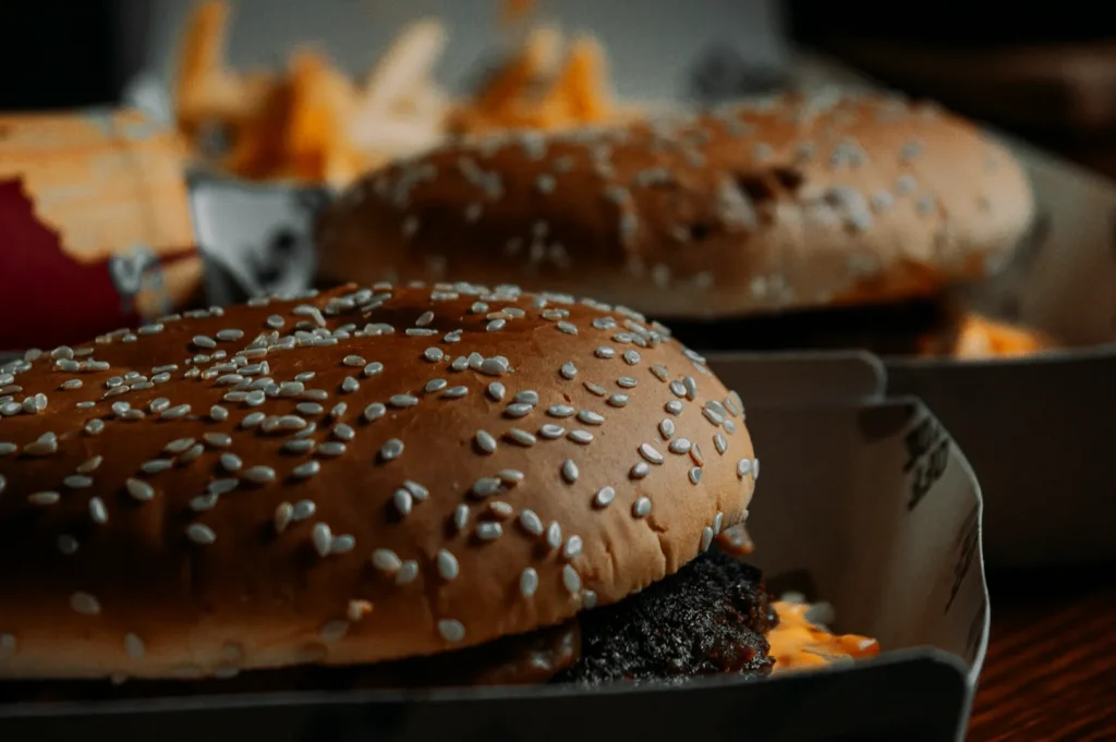Close-up of two sesame seed burgers in boxes, with crisp golden fries in the background, creating a warm and inviting fast-food scene.