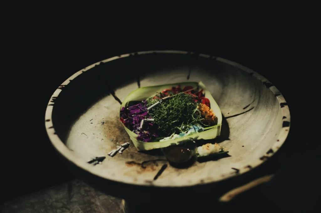 A rustic bowl with colorful vegetables, herbs, and sauce in a banana leaf, evoking a natural, earthy tone against a dark background.