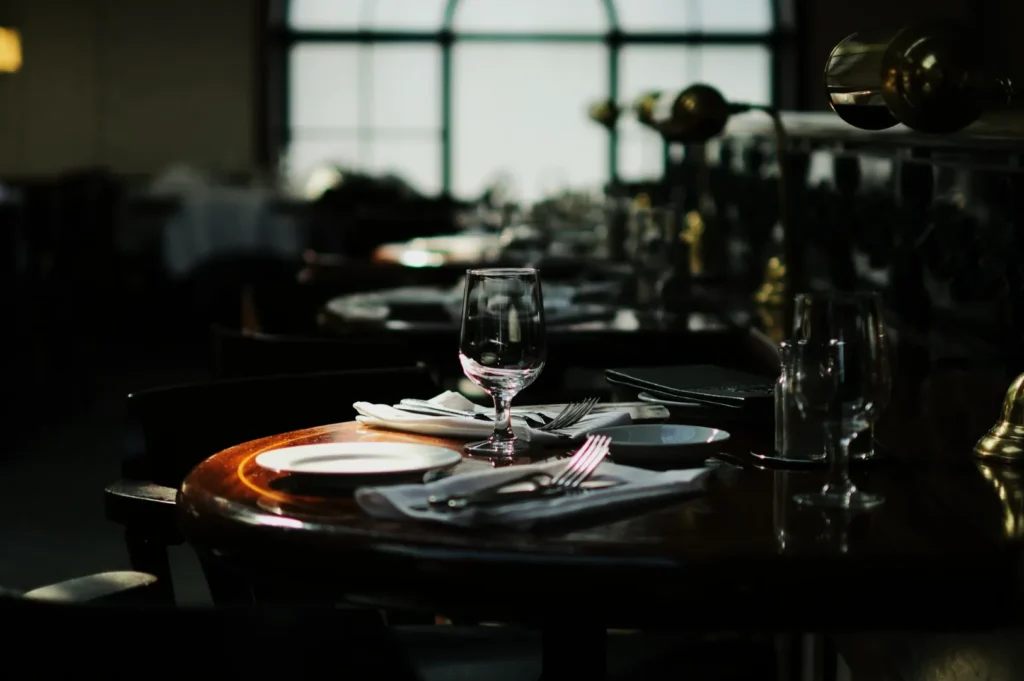 Elegantly set restaurant table with wine glasses, plates, and cutlery. Soft, warm lighting creates an intimate and inviting atmosphere.