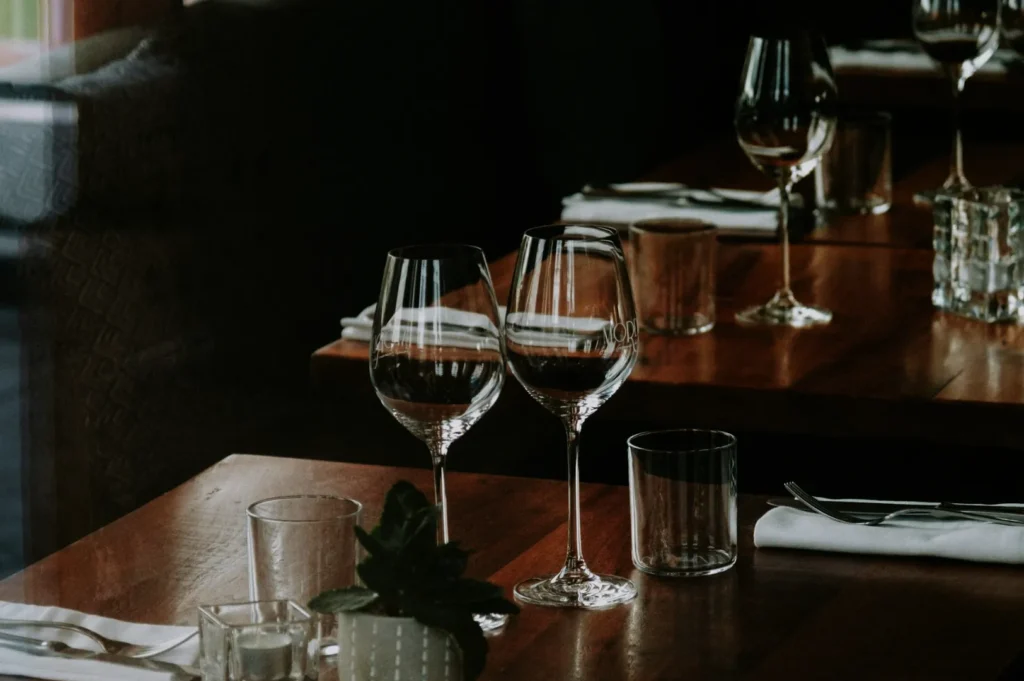 Elegant restaurant table setting with two empty wine glasses, folded napkins, water glass, and candle on a wooden table, conveying a cozy, inviting ambiance.
