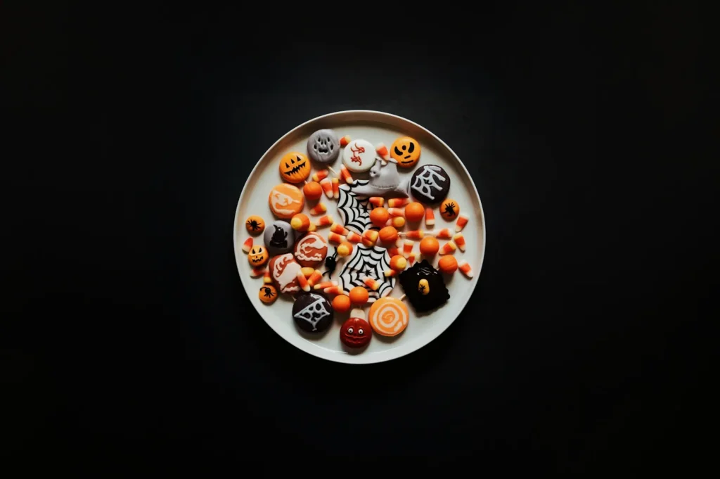 Plate of Halloween-themed cookies and candy corn on a black background. Cookies are decorated with pumpkins, ghosts, and spiderwebs, evoking a festive mood.