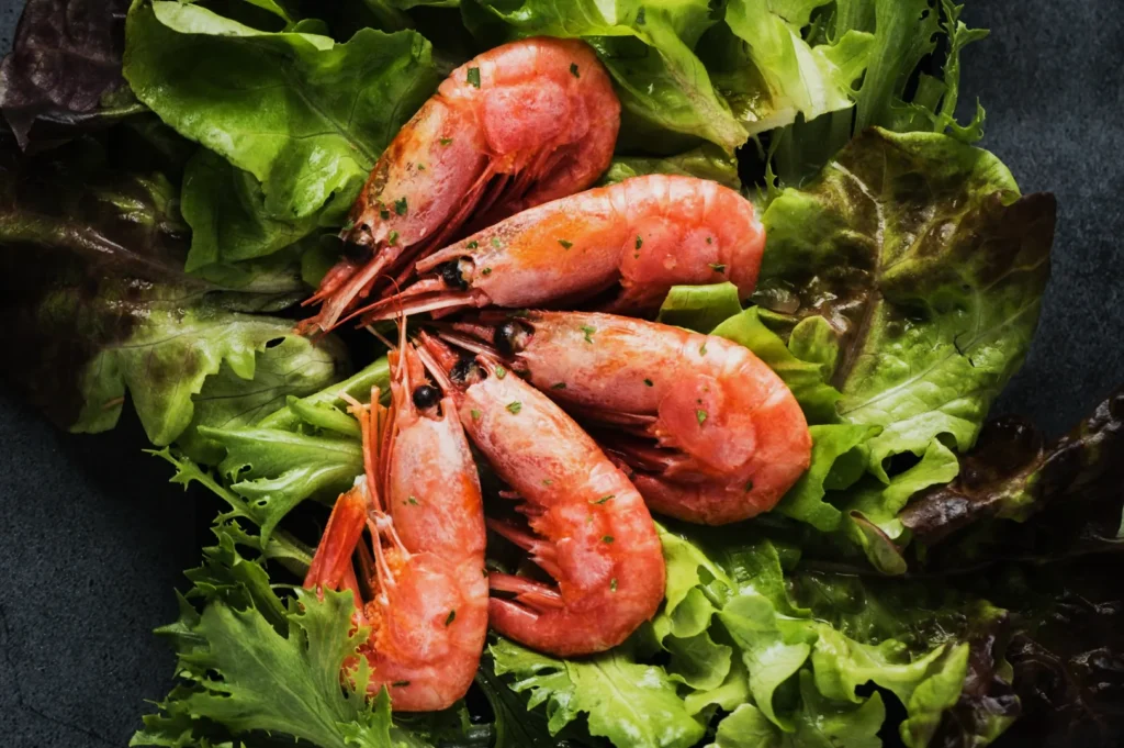 Five pink shrimp arranged on a bed of fresh green and red lettuce. The dish appears fresh and vibrant, evoking a feeling of culinary delight.
