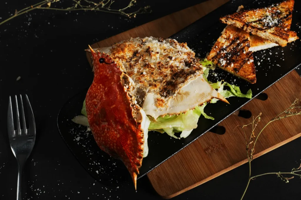 Elegant crab dish with toasted bread on a sleek black platter. Garnished with lettuce and grated cheese, set on a wood board. Sophisticated and inviting.