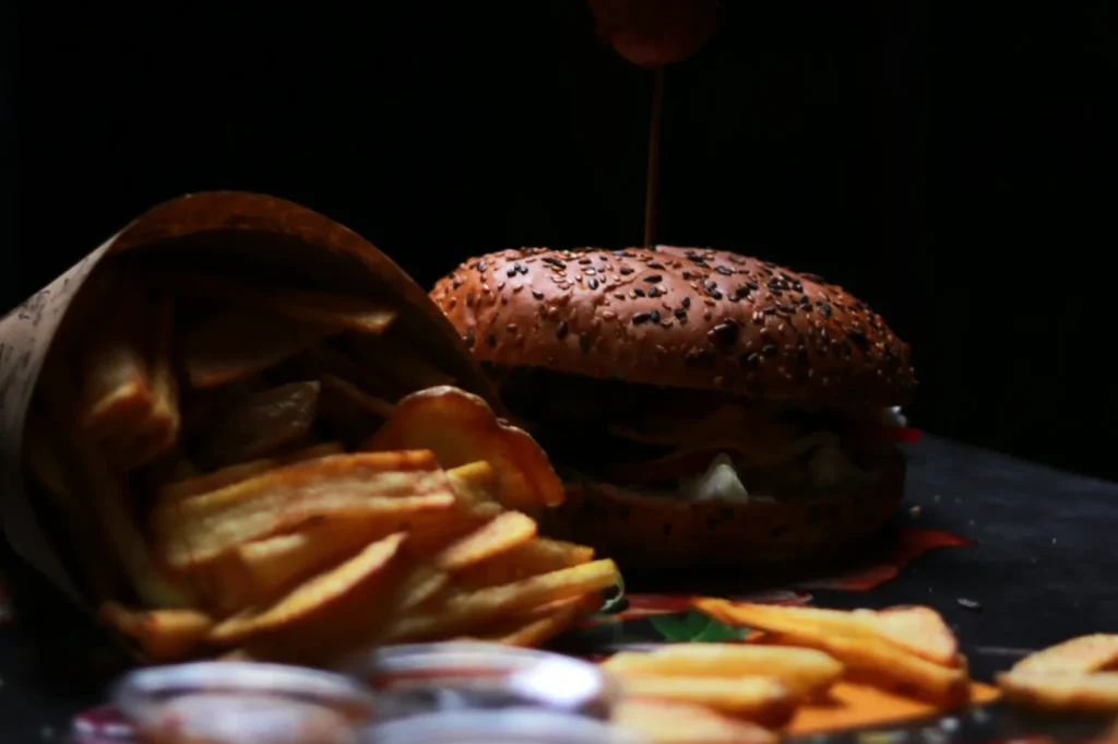Close-up of a sesame seed burger with fresh toppings, next to a paper-wrapped serving of golden fries, creating a rustic and appetizing scene.