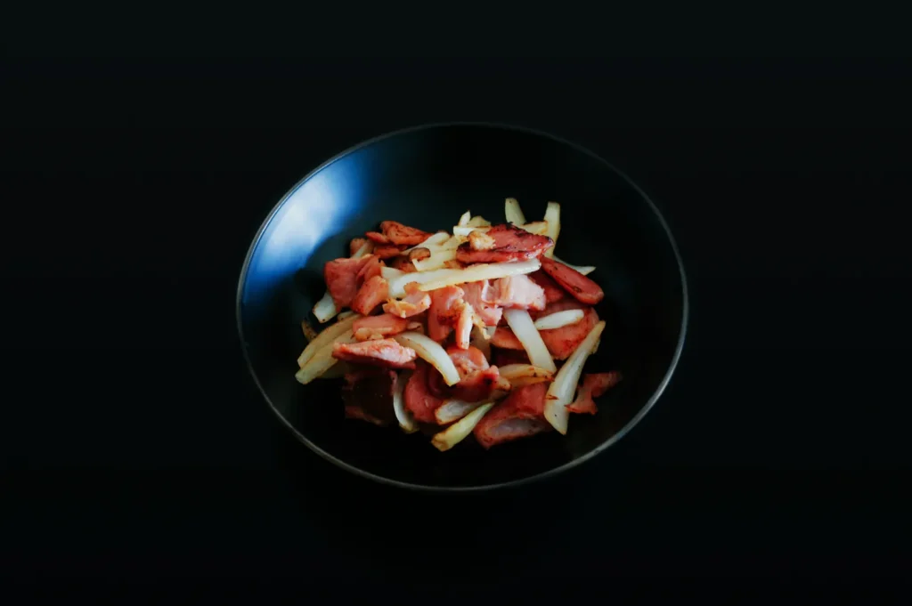 A black bowl of sizzling stir-fried beef and onions sits against a dark background, conveying a warm, appetizing, and savory dish.