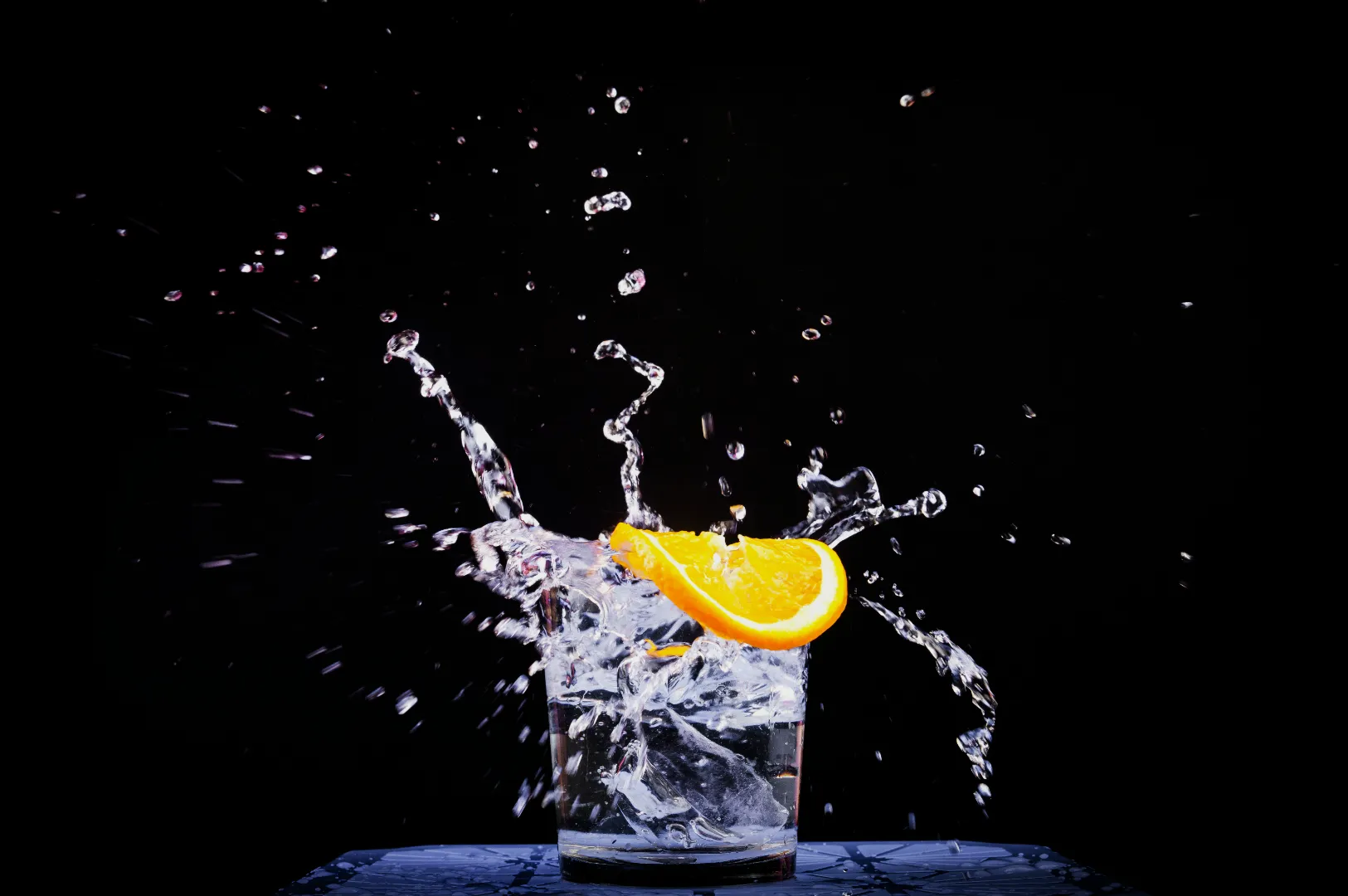 A splash of water erupts from a glass with an orange slice, set against a dark background. Dynamic, refreshing, and vibrant scene.