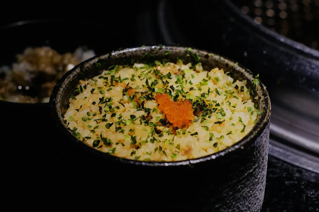 A stone bowl of creamy risotto topped with vibrant orange roe and sprinkled with herbs, set against a dark background, conveying a gourmet and elegant feel.