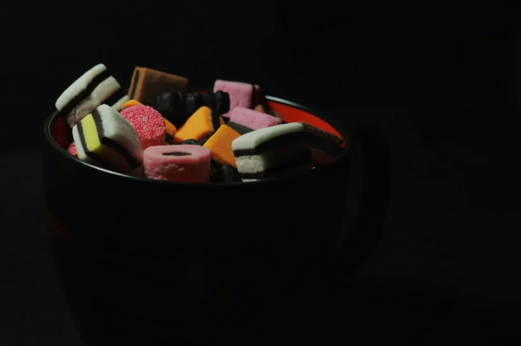 A black cup filled with colorful, assorted licorice allsorts is set against a dark background, highlighting the candies' bright hues and varied textures.
