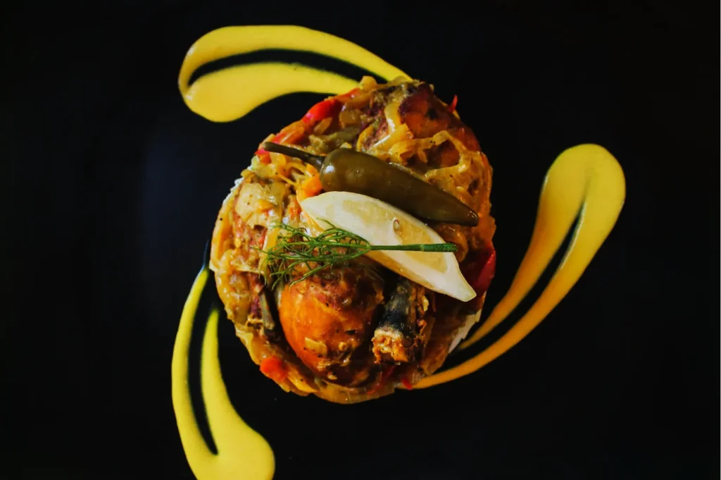 A vibrant dish on a black plate features marinated fish with sliced jalapeño, lemon, and dill garnished with yellow sauce artfully swirled around the plate.