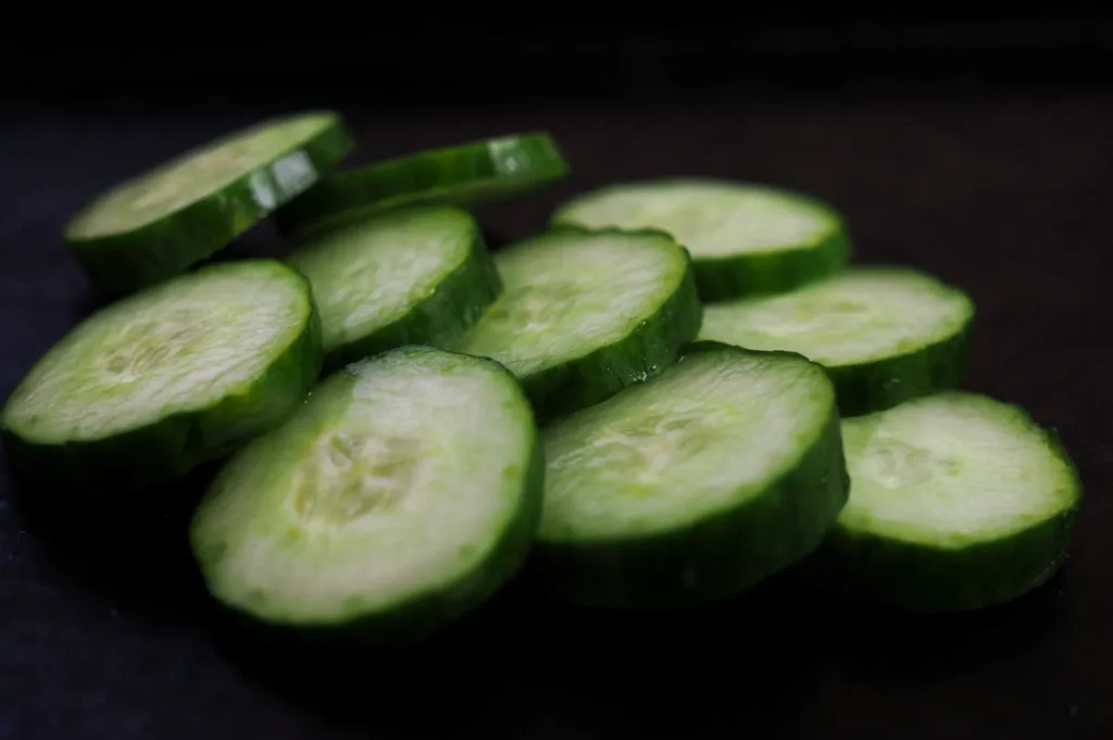 Slices of fresh green cucumber arranged on a dark surface. The cucumber looks crisp and vibrant, conveying freshness and a healthy tone.