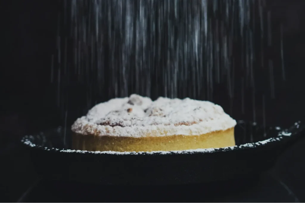A dusting of powdered sugar falls onto a freshly baked pie in a dark setting. The scene conveys a cozy, inviting, and mouth-watering feel.