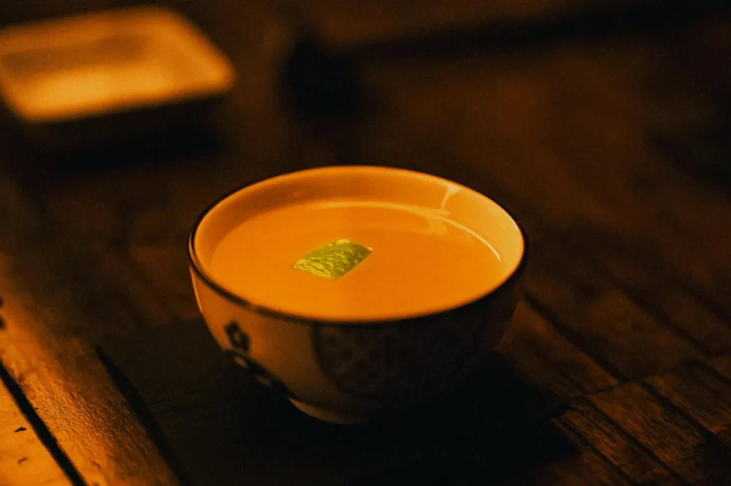 A small, ornate bowl of creamy soup with a garnish, likely a leaf, floats on top. Warm, moody lighting enhances the rustic wooden table beneath.