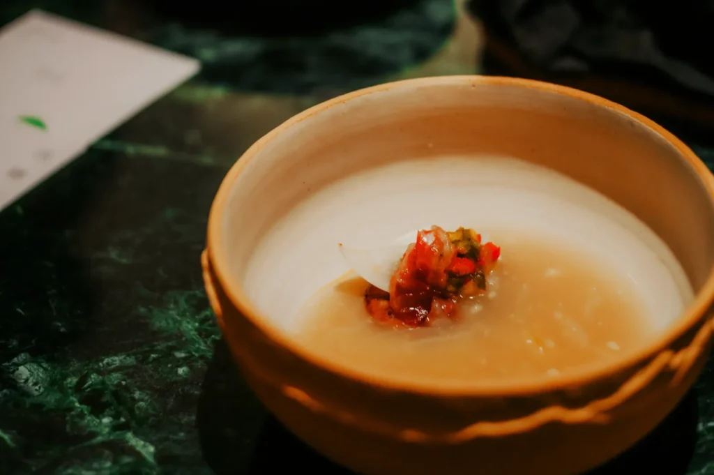 A rustic ceramic bowl filled with creamy soup, topped with vibrant red and green garnish on a dark marble table, conveying an elegant and warm ambiance.