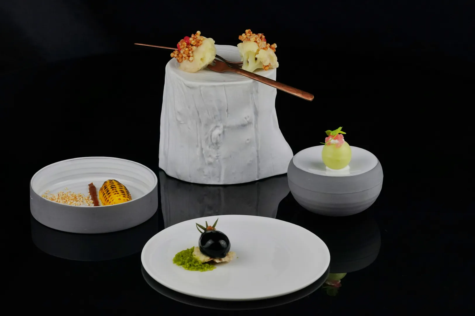 Elegant gourmet dishes on a glossy black surface, featuring artistic presentations on white ceramic. The tone is sophisticated and minimalist.